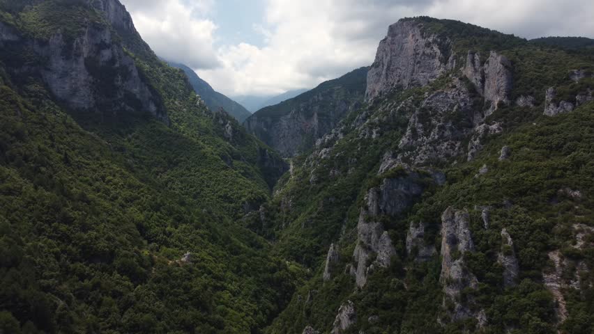 Aerial view showcases the dramatic cliffs of Olympos Mountain with lush greenery of a serene mountain valley. Rugged terrain, untouched wilderness, forest-covered slopes and steep ridges and peaks.