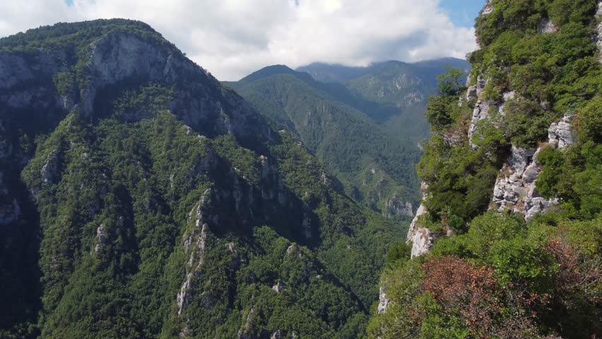 Aerial view showcases the dramatic cliffs of Olympos Mountain with lush greenery of a serene mountain valley. Rugged terrain, untouched wilderness, forest-covered slopes and steep ridges and peaks.