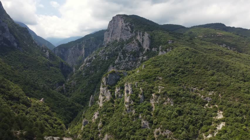 Aerial view showcases the dramatic cliffs of Olympos Mountain with lush greenery of a serene mountain valley. Rugged terrain, untouched wilderness, forest-covered slopes and steep ridges and peaks.