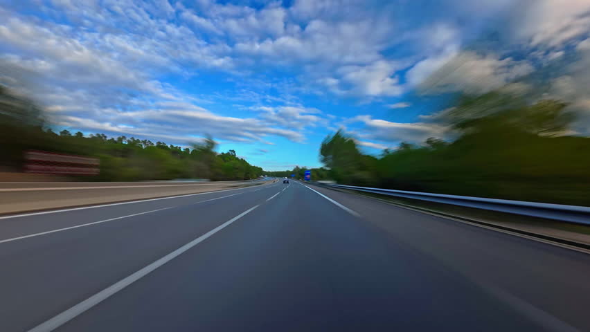 Timelapse of road drive along the highway. Front view to the road and surrounding landscapes. Trees stretch on both sides of road. Fast car hyperlapse. Road trip travel concept sort of dashcam POV