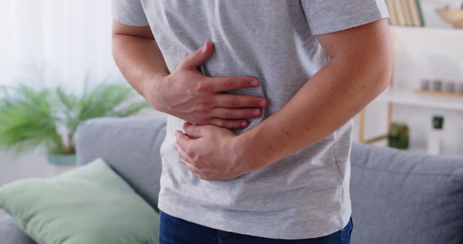 Man having pains in stomach. Young man suffering from a belly ache. Cropped shot of a sick man with an ulcer, IBS, colitis, or dyspepsia holding hands on his abdomen. Health problems concept