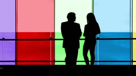 Silhouetted businessman and woman meet against a backdrop of multicolored windows, then walk off camera together.