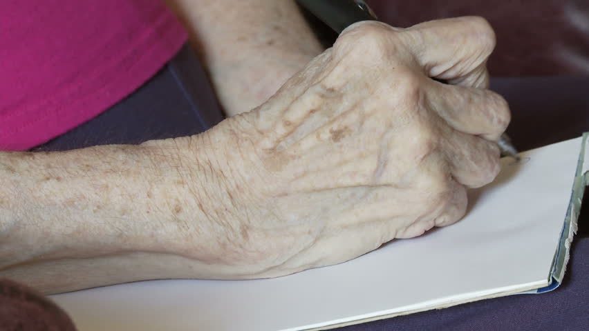 Elderly woman's hands, crippled with arthritis, write a letter on a pad.