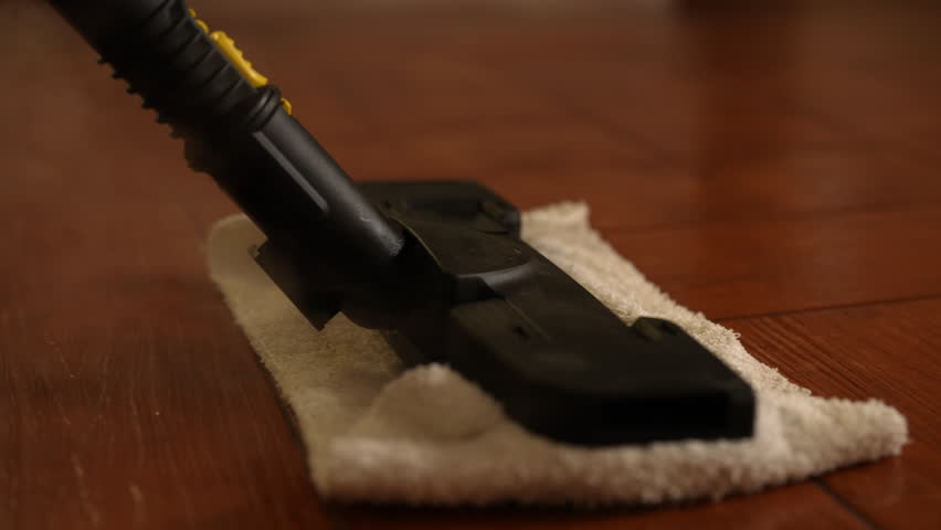 Detail shot of unrecognizable person using modern steam cleaner to sanitize wooden floor with microfiber cloth attached, emitting steam for deep cleaning and disinfection, closeup, slow motion.