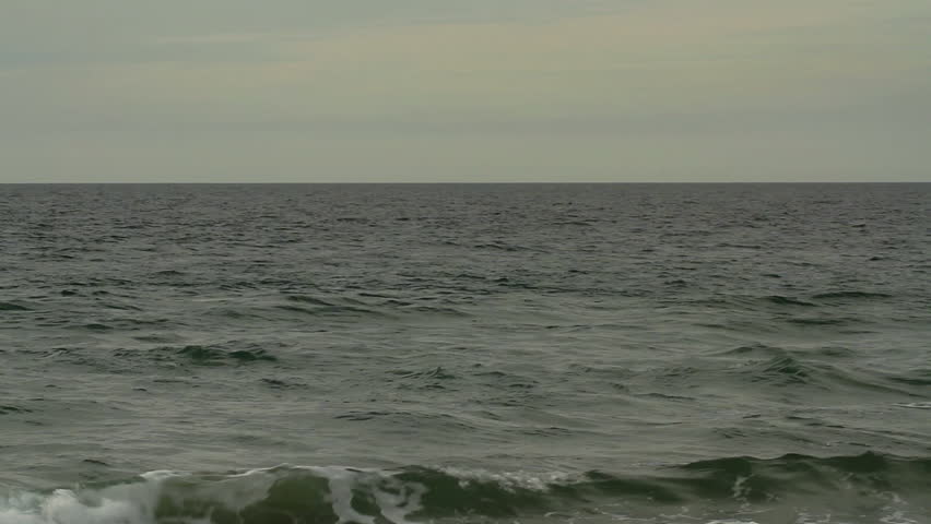 Pelican flying low over the Pacific Ocean. Camera pans with the bird.