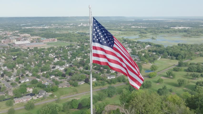 Profile view of American flag at Grandad Bluff bluff overlooking the city of La Crosse, the Mississippi River Valley, Wisconsin in USA. Drone view.