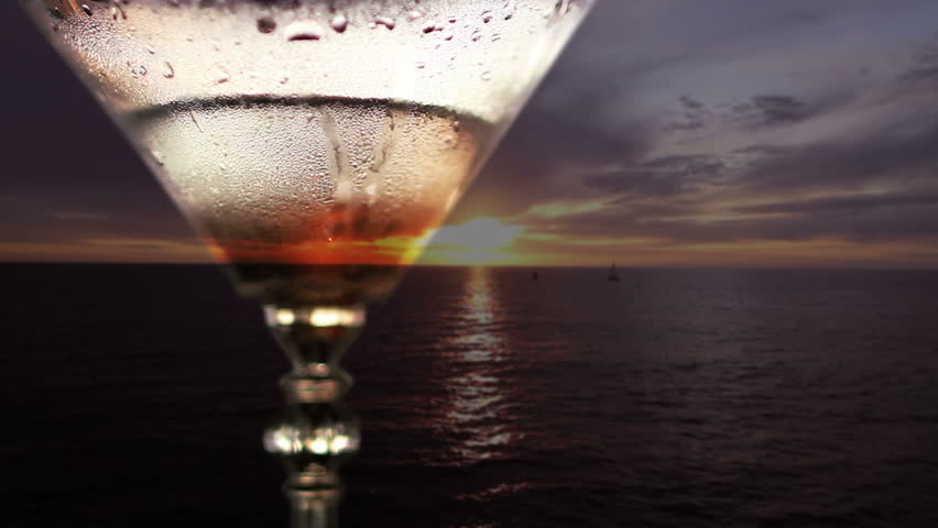 Sunset seen through a martini glass. An olive is dropped into the drink.
