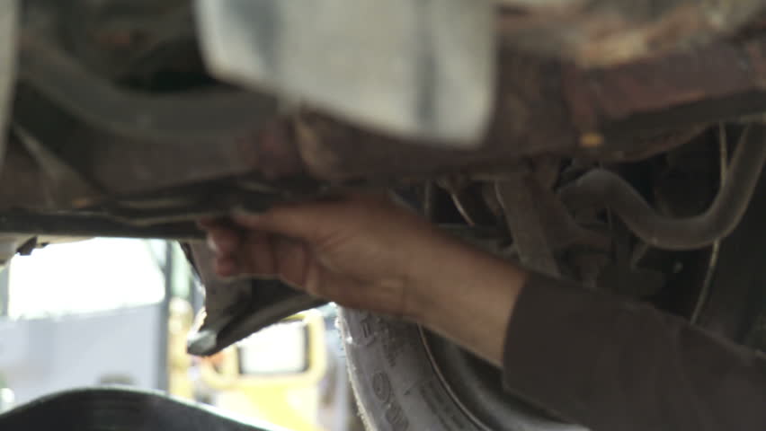 Auto mechanic drains off the oil from an old car. Detail shot with hand undoing