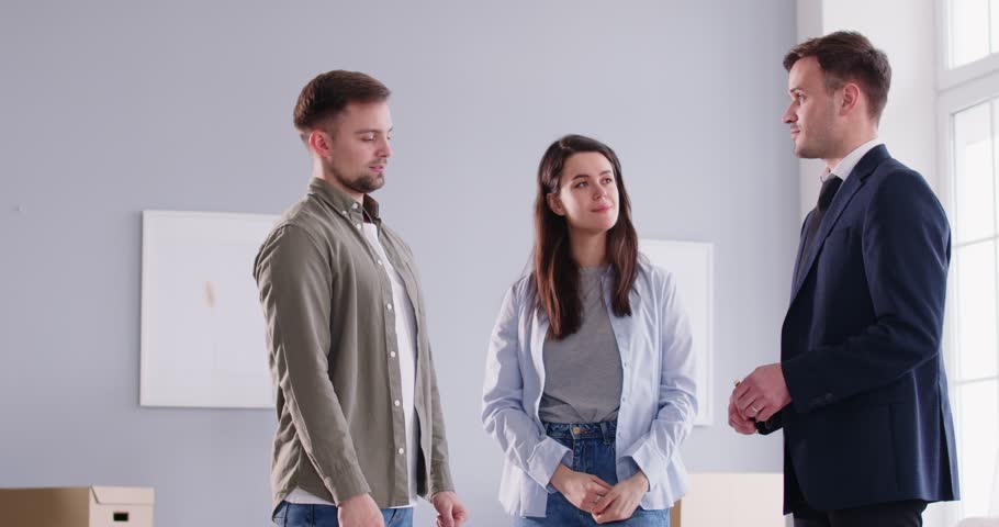 Happy family couple buying a new house or apartment together. Young married man and woman meet with their real estate agent, sign a contract agreement and exchange handshakes