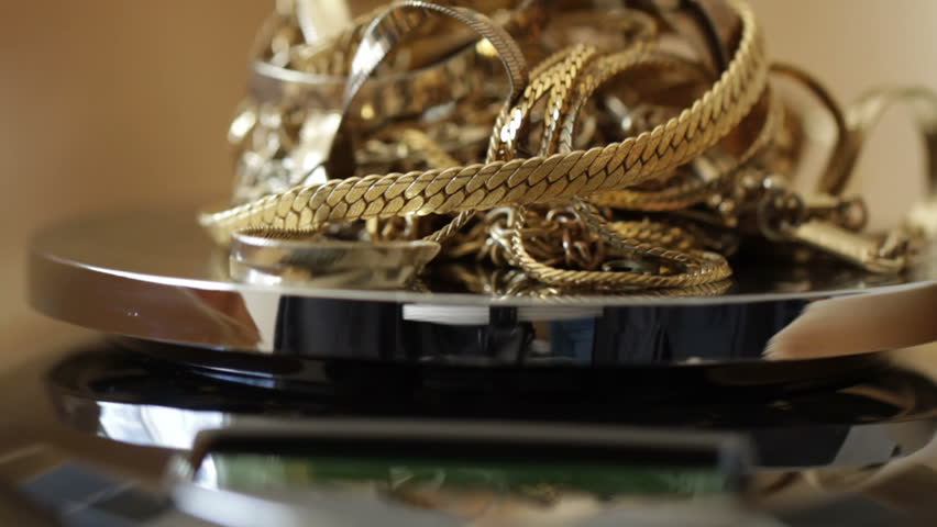 Gold jewelry piled on scales with a gold backdrop. Shallow focus with camera