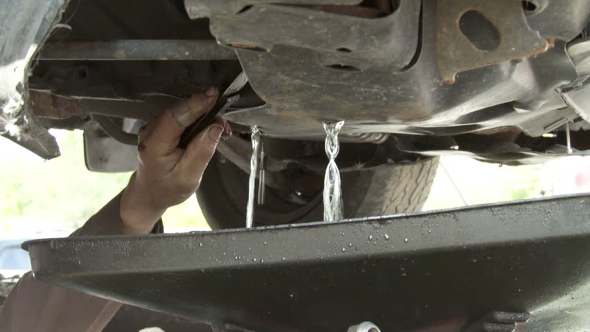 Auto mechanic drains off water and anti-freeze from an old car. Detail shot.