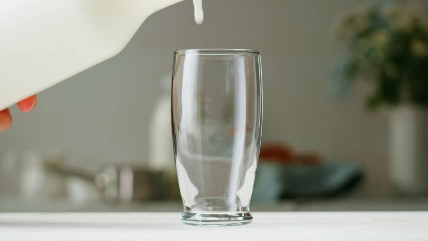 Milk pouring in glass cup close-up. Glass with yogurt, dairy products concept. Drinking fresh lactose-free milk in morning.