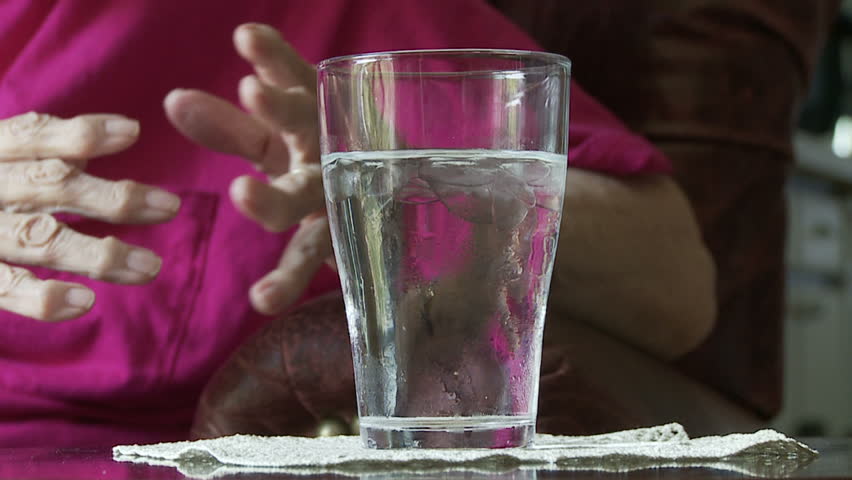 Elderly woman's hands, crippled with arthritis, pick up a glass of iced water to