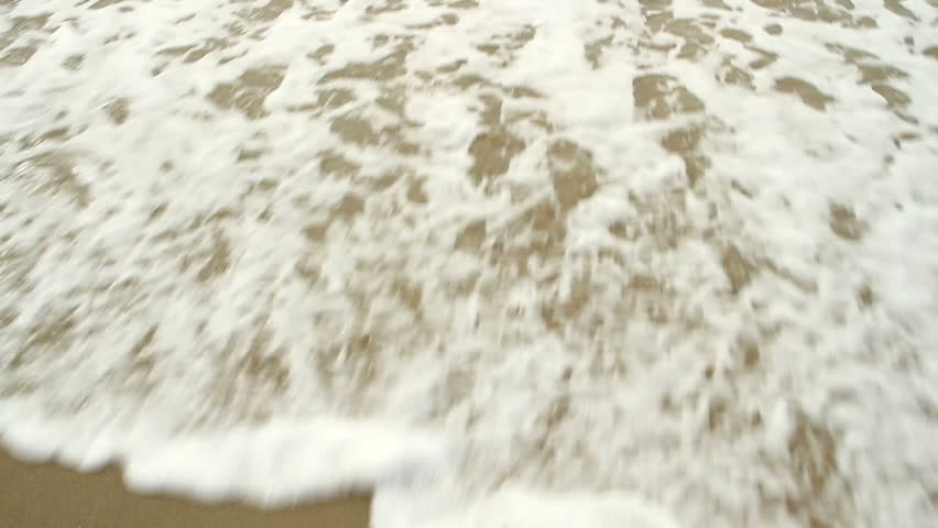 Sea water washes up a sandy shore and out again. Loopable clip.