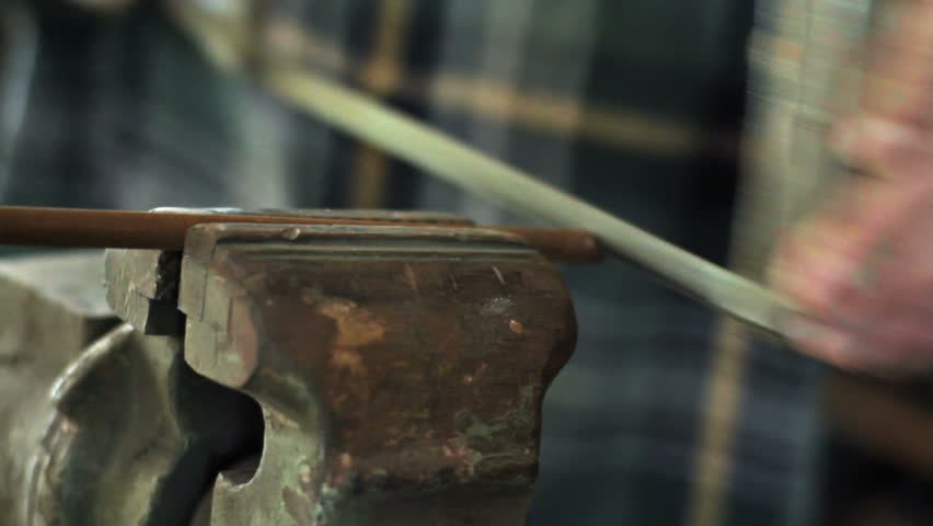 Detail of hacksaw cutting through a piece of steel rod held in a workshop vice.