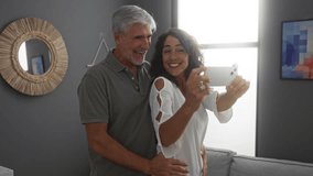 Couple taking selfie in cozy apartment shows love and happiness of middle-aged man and woman together indoors in stylish living room embracing and smiling joyfully - Powered by Shutterstock - Get 15% off with code: PIKWIZARD15