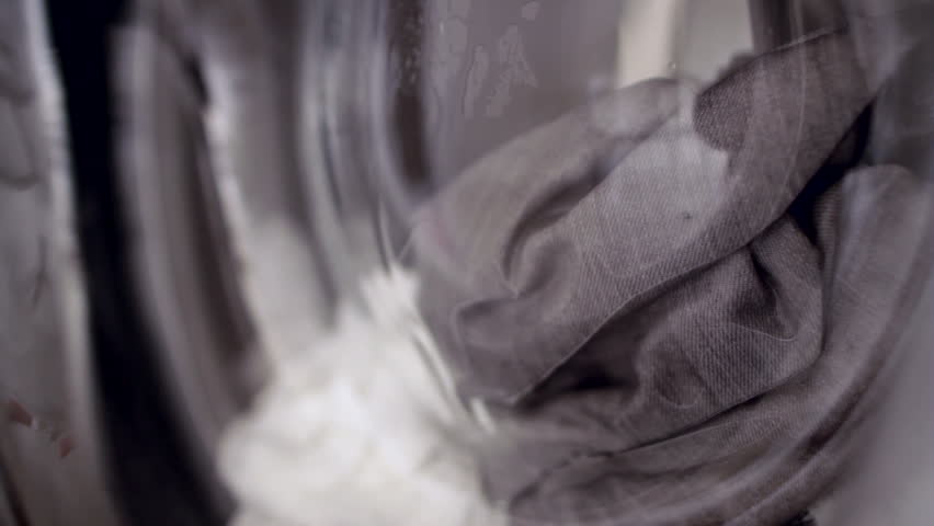 Tight shot of clothes in washing machine as they soak and then spin.