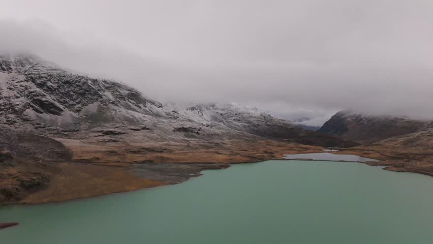 Flying over Lago di Bianco,turquoise lake reflecting snowy peaks and clouds in the swiss alps, creating a tranquil and captivating winter landscape Graubünden, Switzerland