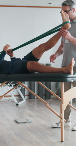 Mature man, physiotherapist and leg with resistance band for stretching, muscle recovery or physical therapy. Male person, orthopedic and client lying on bed with elastic for relief or physiotherapy