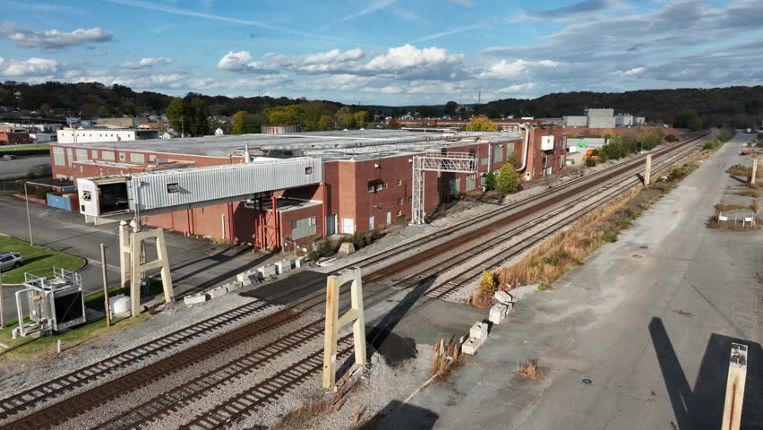 Aerial view of red brick factory beside tracks of railway during sunset time in industrial area of american town. Colorful forest landscape in background. Wide shot.