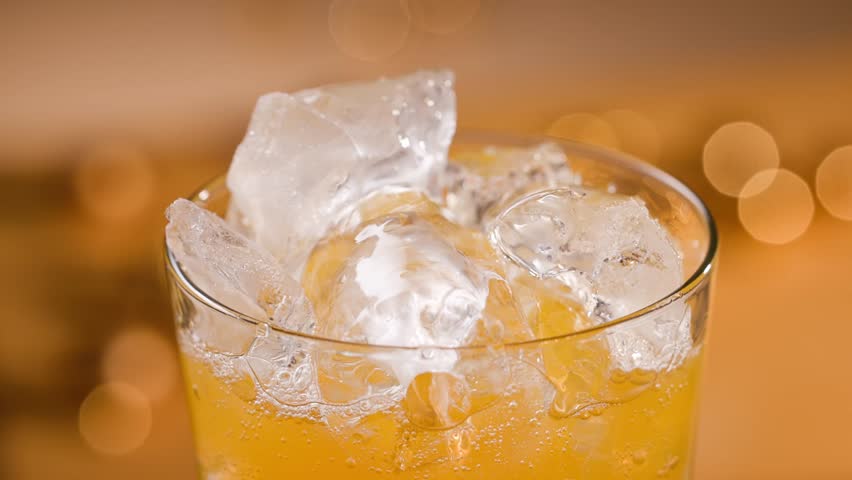 fresh sparkling orange drink in glass with ice, close up. Defocused orange festive background