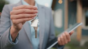 Camera focus on real estate agent holding keys to house with one hand. Person in grey suit in blurred background. Holding notepad with other hand. Property for sale. Offering purchase. - Powered by Shutterstock - Get 15% off with code: PIKWIZARD15