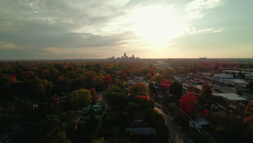 An aerial shot of the Indianapolis skyline, with vibrant autumn trees and neighborhoods illuminated by a glowing sunrise.