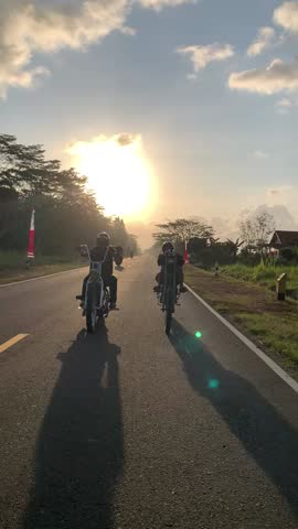 Two young men ride a motorcycle under the sunset