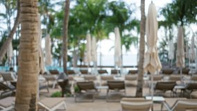 Blurred view of a tropical resort with defocused palm trees, sun loungers, umbrellas, and a man in the background, creating a serene vacation ambiance with out of focus scene. - Powered by Shutterstock - Get 15% off with code: PIKWIZARD15