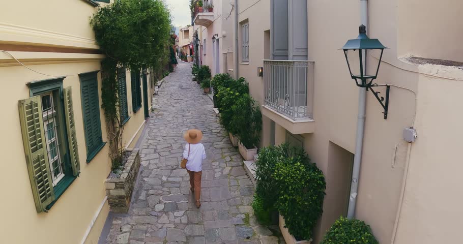 Tourist woman with hat walking sightseeing an beautiful street in the old district of Plaka in Athens, Greece, aerial drone tracking shot