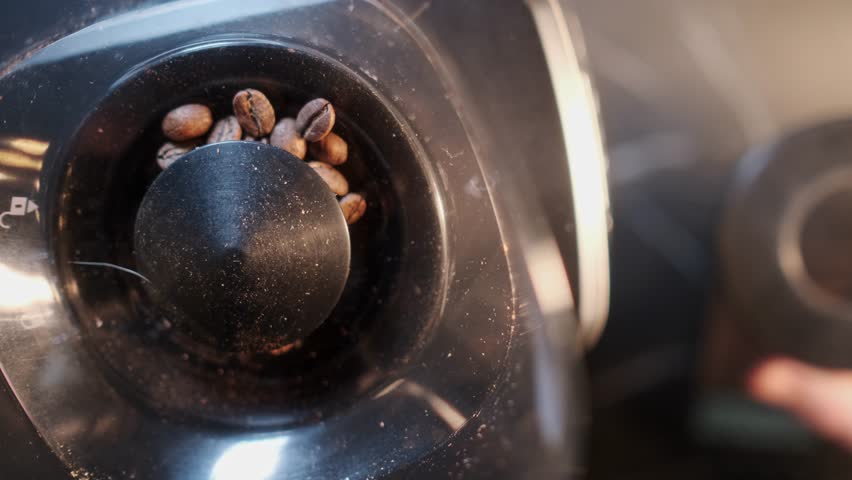 Slow motion close-up video of pouring coffee beans into a glass bowl. A professional barista pours coffee into a coffee grinder. High quality 4k footage