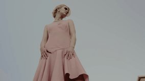 Low angle view of a confident woman in a stylish pink dress and pearl necklace, posing outdoors against a clear sky. Confident Woman Posing in Pink Dress with Pearl Necklace Outdoor - Powered by Shutterstock - Get 15% off with code: PIKWIZARD15