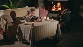 Teenage girl writing a greeting card near a glowing fireplace while a cute Golden Retriever playfully runs around. Cozy evening before winter holidays. High quality 4k footage - Powered by Shutterstock - Get 15% off with code: PIKWIZARD15