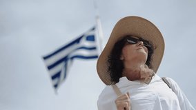 Fashion hispanic woman in Athens, greek flag waving on pole at ancient Acropolis on column against blue sky background, spring sunny day, slow motion - Powered by Shutterstock - Get 15% off with code: PIKWIZARD15