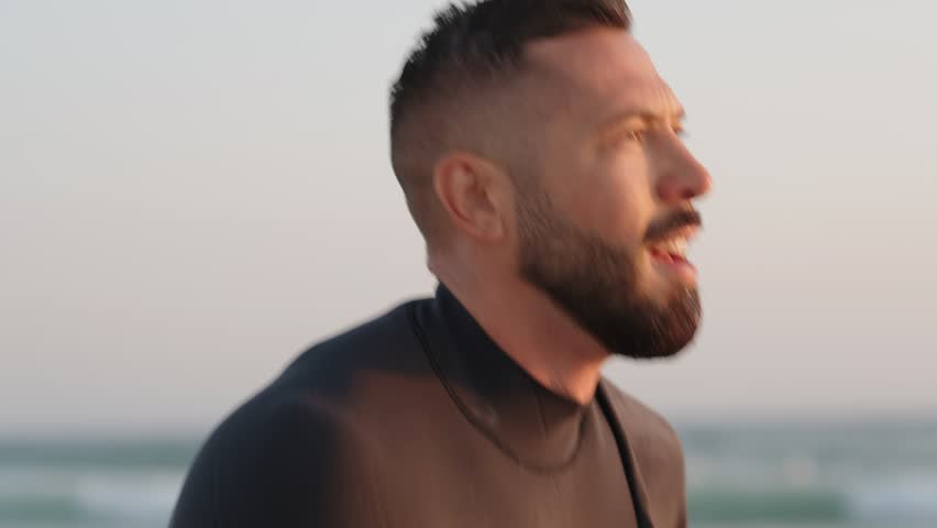 Tired male surfer catching his breath after a surf session. He looks out to the waves, contemplating his next ride as the sun sets behind him.