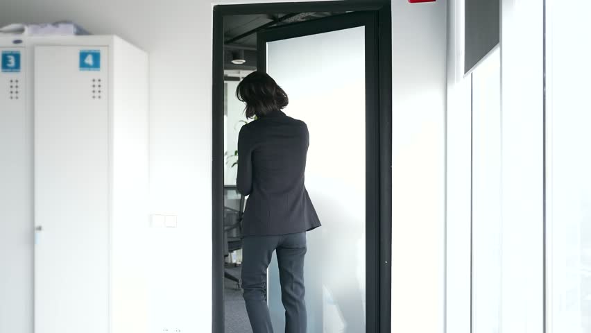 Back view of businesswoman entering modern office room through glass door. Worker making entrance. Concept of professional woman in corporate environment, workplace dynamics, and office life