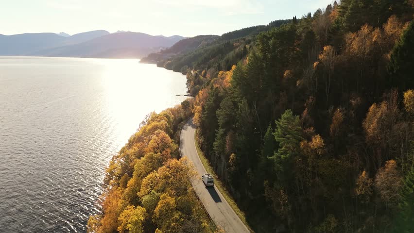 Campervan drives near majestic Norway lake in autumn season, aerial view