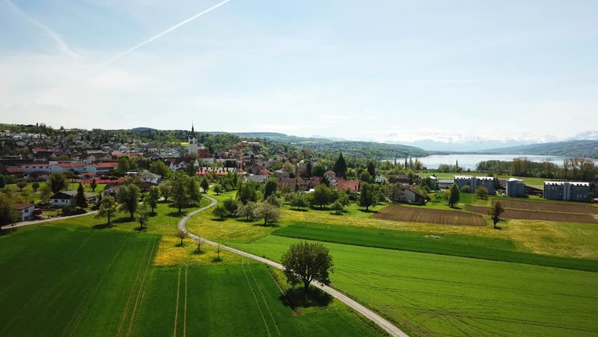 Aerial view of swiss landscape with cultivated fields, Seengen village and a lake (Hallwilersee) in the background, Aargau, Switzerland, drone flying over