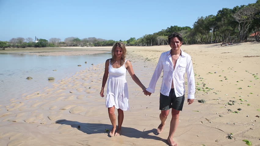 Happy couple holding by hands and walking together at beach