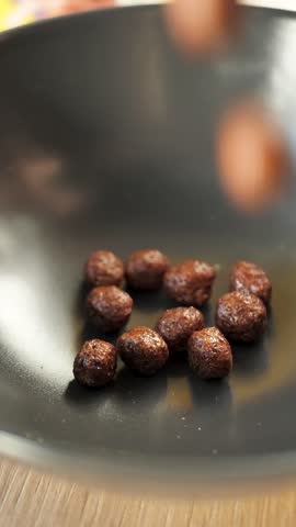 Vertical video of chocolate cereal balls falling into a bowl slow motion. Drop cocoa balls into a bowl and add milk. Healthy brown cornflakes in the shape of balls. Snack for kids for breakfast