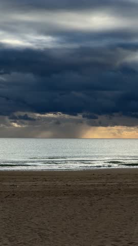 Dramatic cloudy sky over calm ocean waves with golden light peeking through. Vertical video