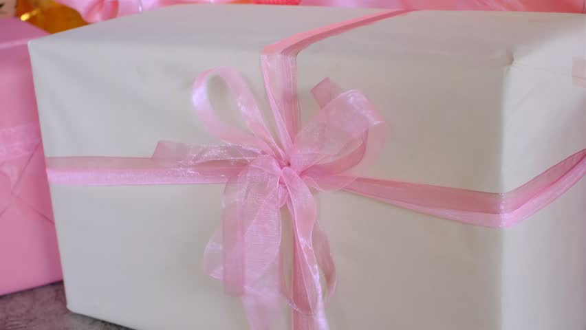 A white box with a pink ribbon tied around it. The box is sitting on a table