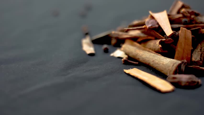 Close-Up Shot of Raw Indian Spices on a Shiny Black Surface: Featuring Cardamom, Cinnamon Stick, Black Pepper, Star Anise, Clove, and More