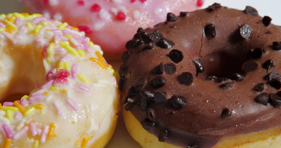 Tasty Donuts Rotation on a White Background. Unhealthy Sweet Food Dessert. Chocolate Doughnut With Christmas Multicolor Sprinkling on a White Fondant Icing