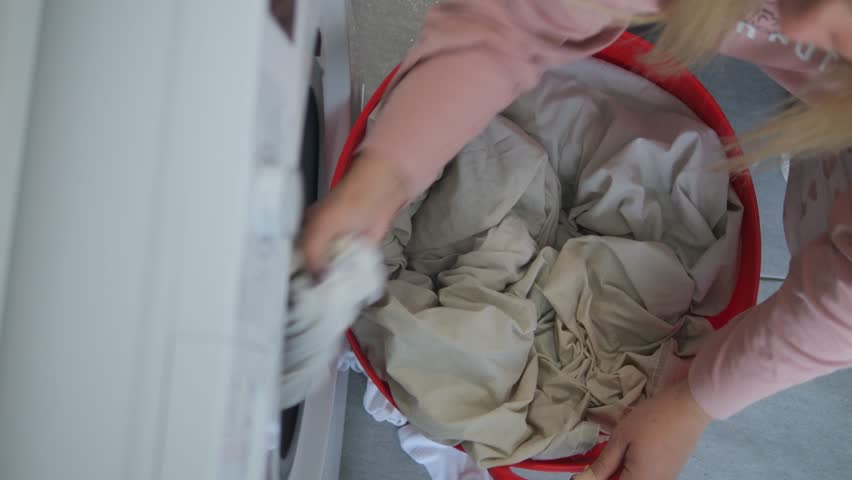 Woman taking white bed linen out of the washing machine. Zenithal view