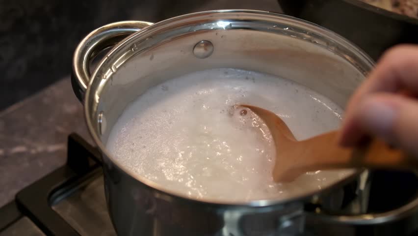 Cooking rice in a steel pot, stirring rice in boiling water.