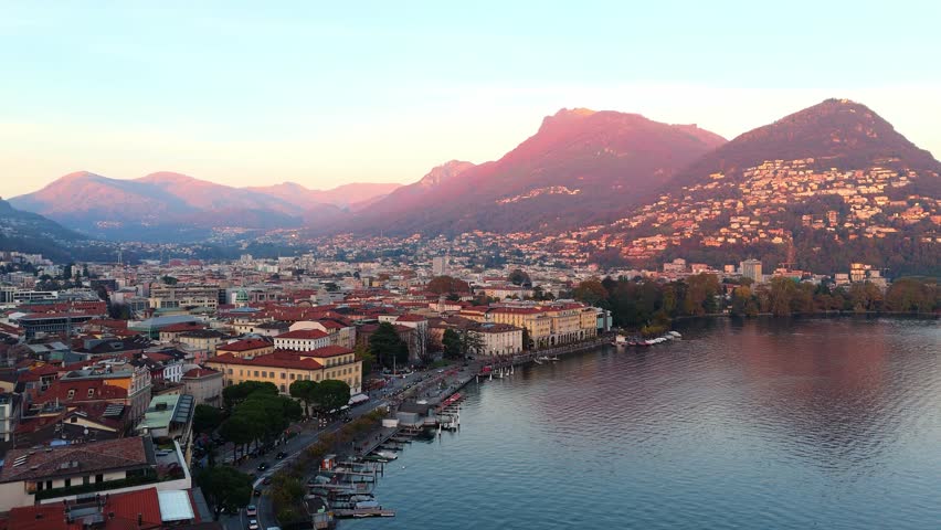 Lugano, switzerland at sunset with city buildings, mountains, and calm lake, aerial view