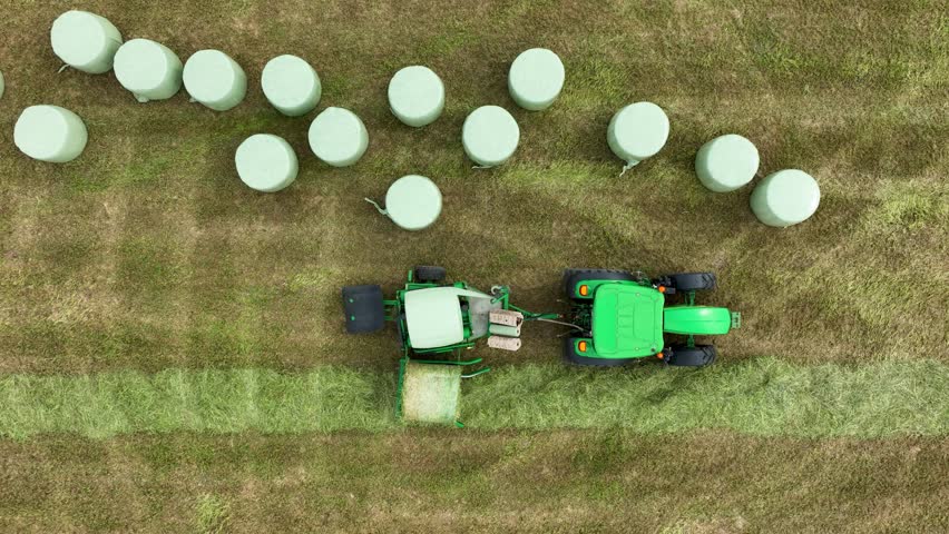 Top down drone view of green tractor in farm land wrapping hay bales in plastic