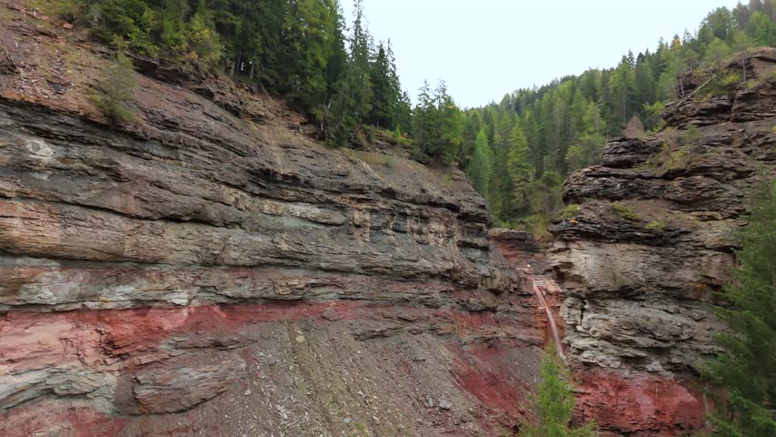 Colorful layered rock formations in Bletterbach Gorge, South Tyrol, Italy, showcasing impressive geological layers. Dense green forest lines the rugged canyon walls in this scenic landscape.