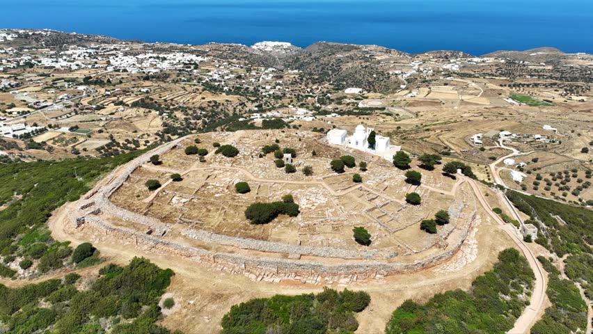 Aerial drone cinematic video of archaeological site of the Mycenaean Citadel and chapel of Agios Andreas built on top of hill overlooking the Aegean sea, Sifnos island, Cyclades, Greece